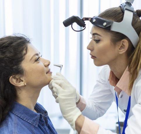 Doctor otorhinolaryngologist checking nose with otoscope of patient at hospital. Nasal congestion, sinusitis, allergy concept.